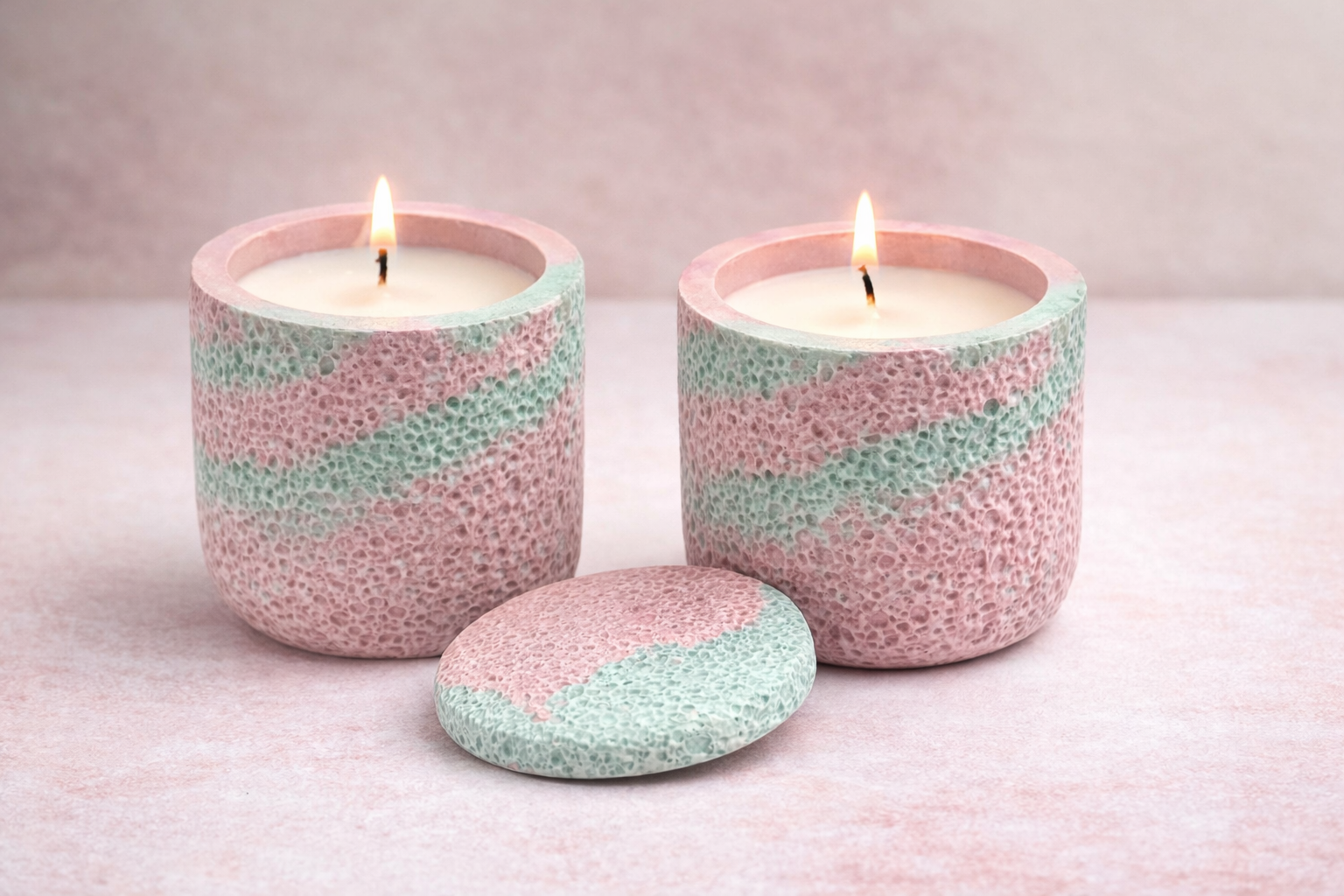 Two pink and blue striped candles with a small stone on a light pink background