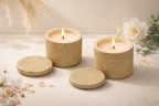Two textured candles in decorative containers with floral elements on a light background
